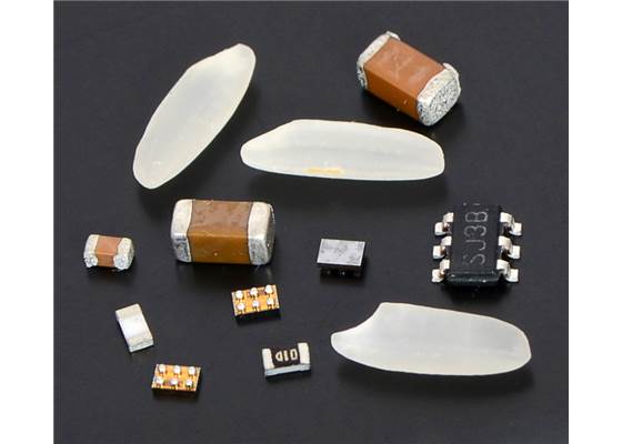 Three FPF1320 BGA parts (two with solder balls facing up) among grains of rice and components in 0603, 1206, and SOT-23 packages.